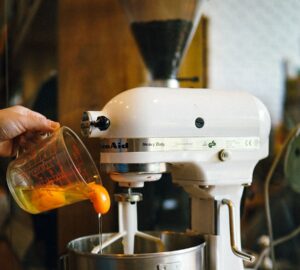 person pouring egg yolks on white stand mixer
