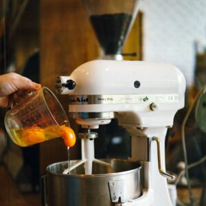 person pouring egg yolks on white stand mixer