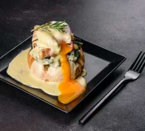 Eggs benedict or eggs florentine on a black plate in the cafe