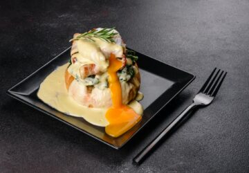 Eggs benedict or eggs florentine on a black plate in the cafe