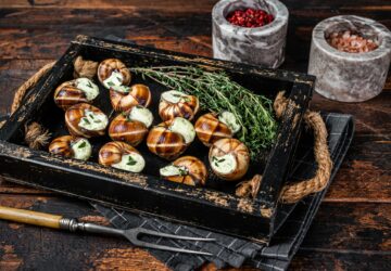 French gourmet - Escargot Snails with garlic butter in a wooden tray. Wooden background. Top view