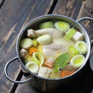 Cooking pot with raw corn-fed chicken, onion, herbs and greens