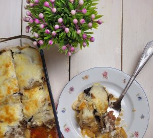 A top view of homemade moussaka served in a glass container and on a decorative plate with a red checkered napkin.