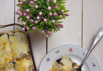 A top view of homemade moussaka served in a glass container and on a decorative plate with a red checkered napkin.