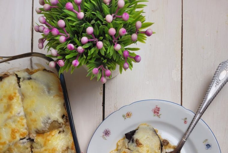 A top view of homemade moussaka served in a glass container and on a decorative plate with a red checkered napkin.